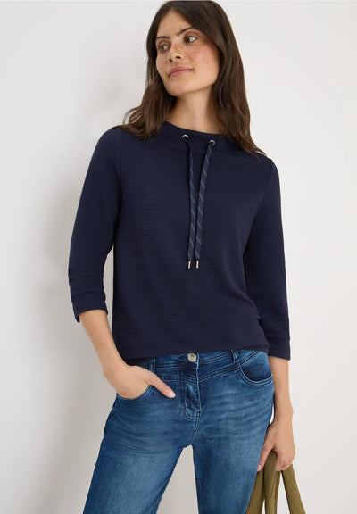 Woman wearing a navy blue hoodie and blue jeans against a white background