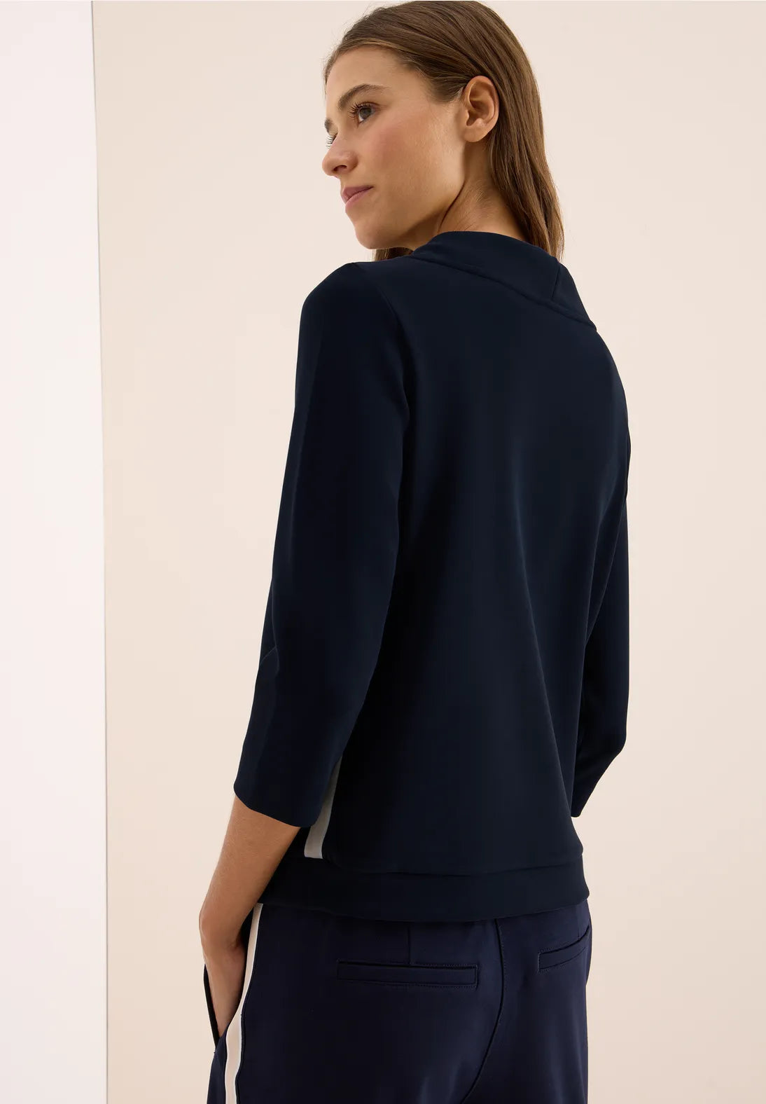 Woman wearing a navy blue sweater and pants against a beige background
