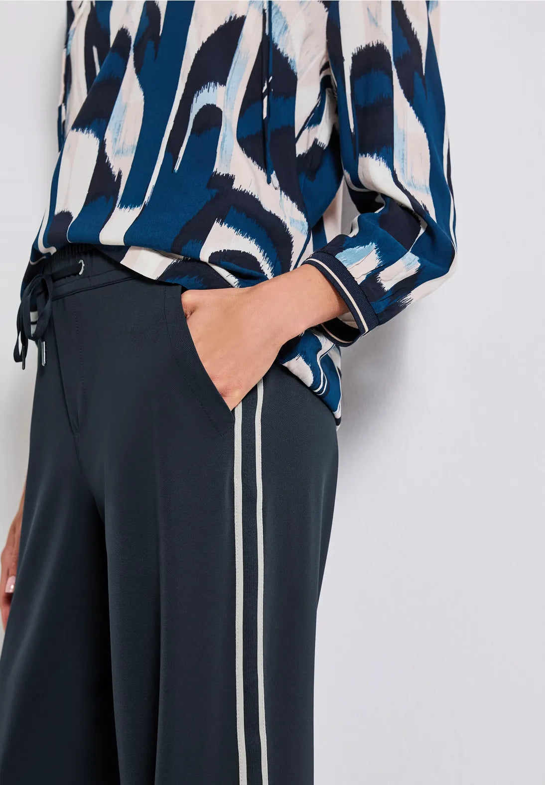 Person wearing a blue and white patterned top with black pants on a light gray background