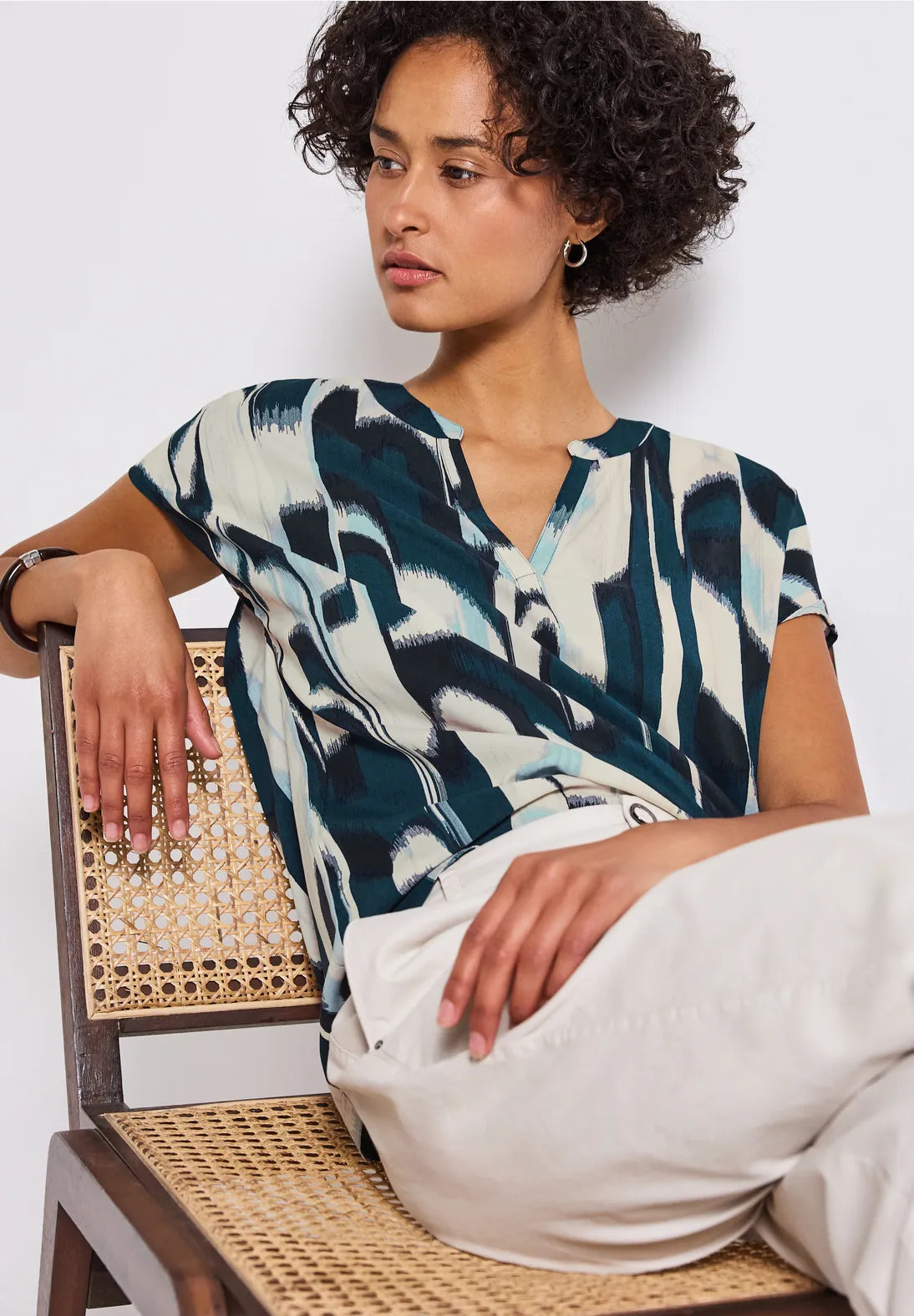 Woman wearing a patterned top sitting on a chair with a white background