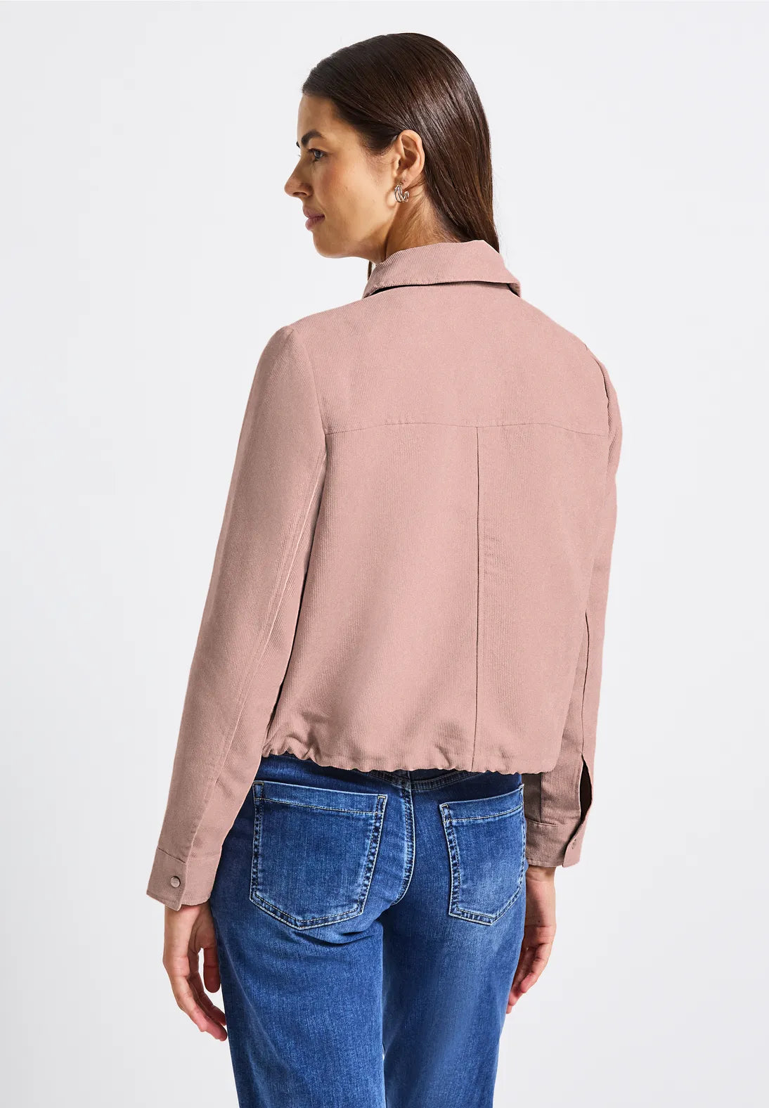 Woman wearing a pink jacket and blue jeans on a white background