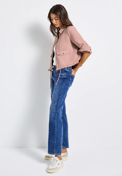 Woman wearing a pink jacket and blue jeans against a white background