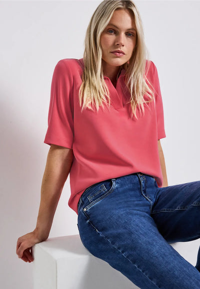 Woman wearing a pink top and blue jeans sitting on a white surface with a light gray background