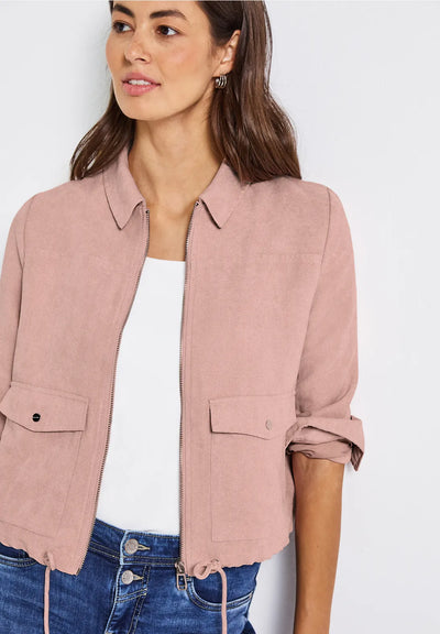 Woman wearing a pink jacket over a white shirt and blue jeans on a light gray background