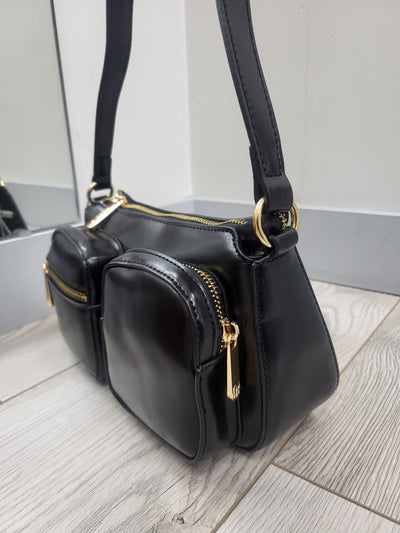 Black handbag with gold zippers on a light wooden floor