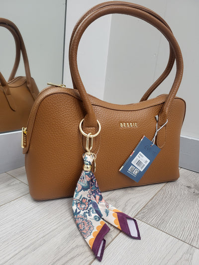 Brown handbag with a floral strap on a light wooden floor