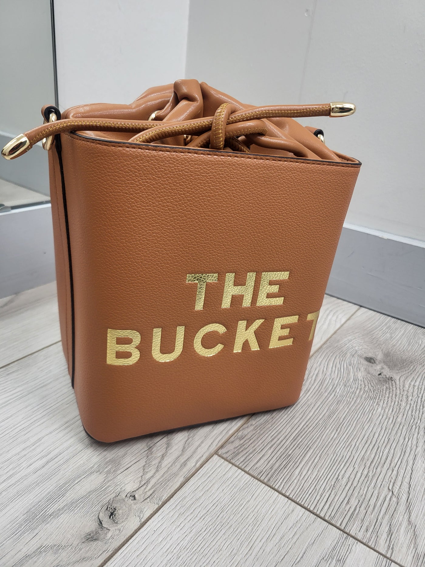 Brown leather bag with 'THE BUCKEY' text on a wooden floor.