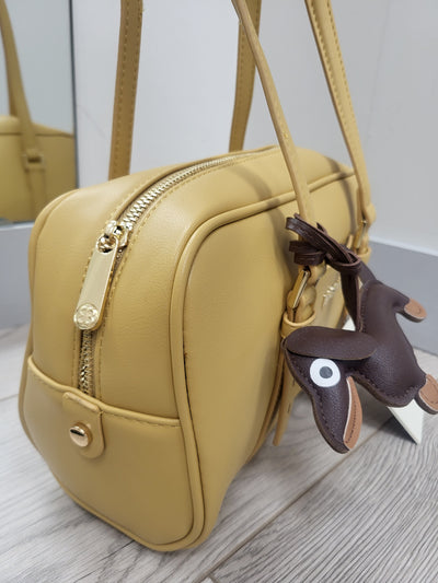 Beige handbag with a small brown dog-shaped keychain on a light wooden surface.