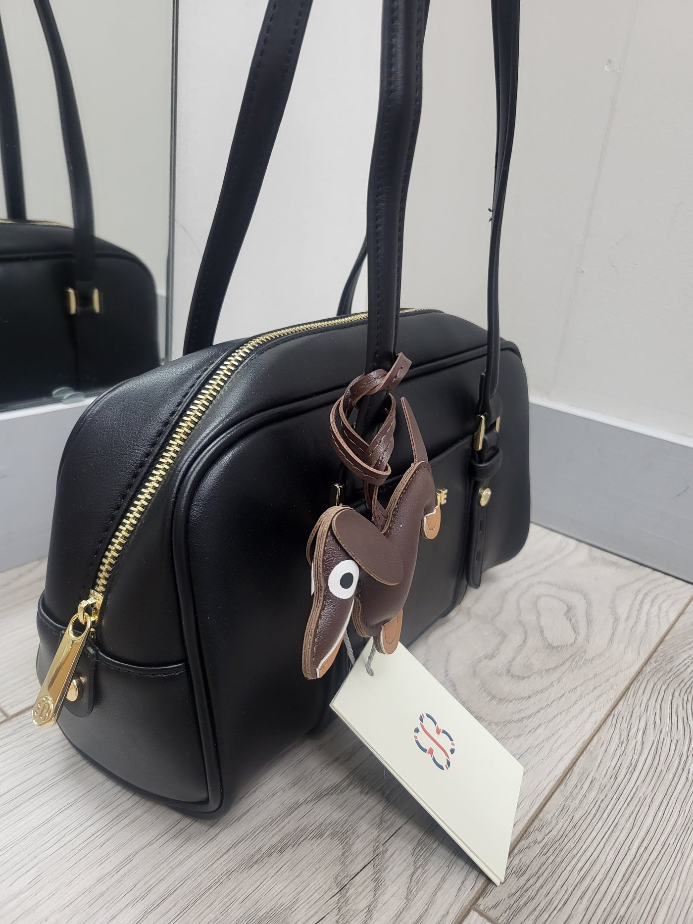 Black handbag with gold zipper and decorative elements on a light wooden surface