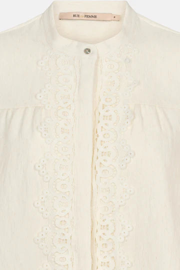 Close-up of a cream-colored blouse with intricate lace detailing on a white background.