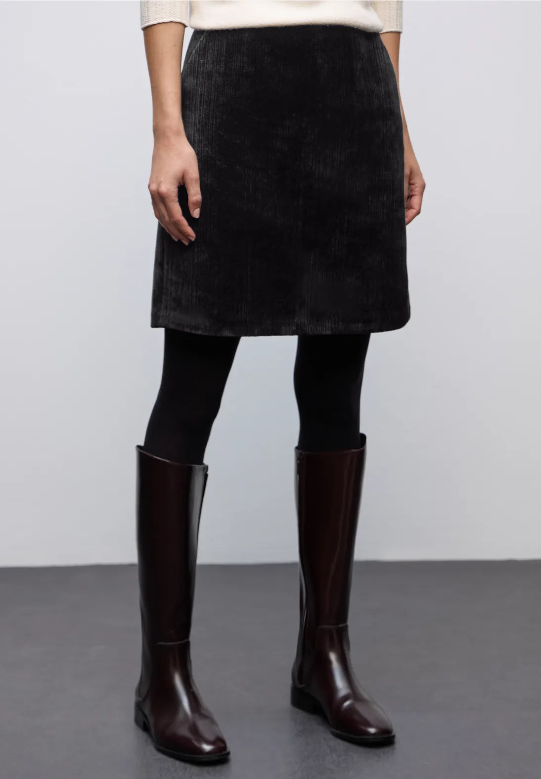 Person wearing a black skirt and brown knee-high boots on a plain background