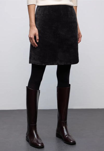 Person wearing a black skirt and brown knee-high boots on a plain background