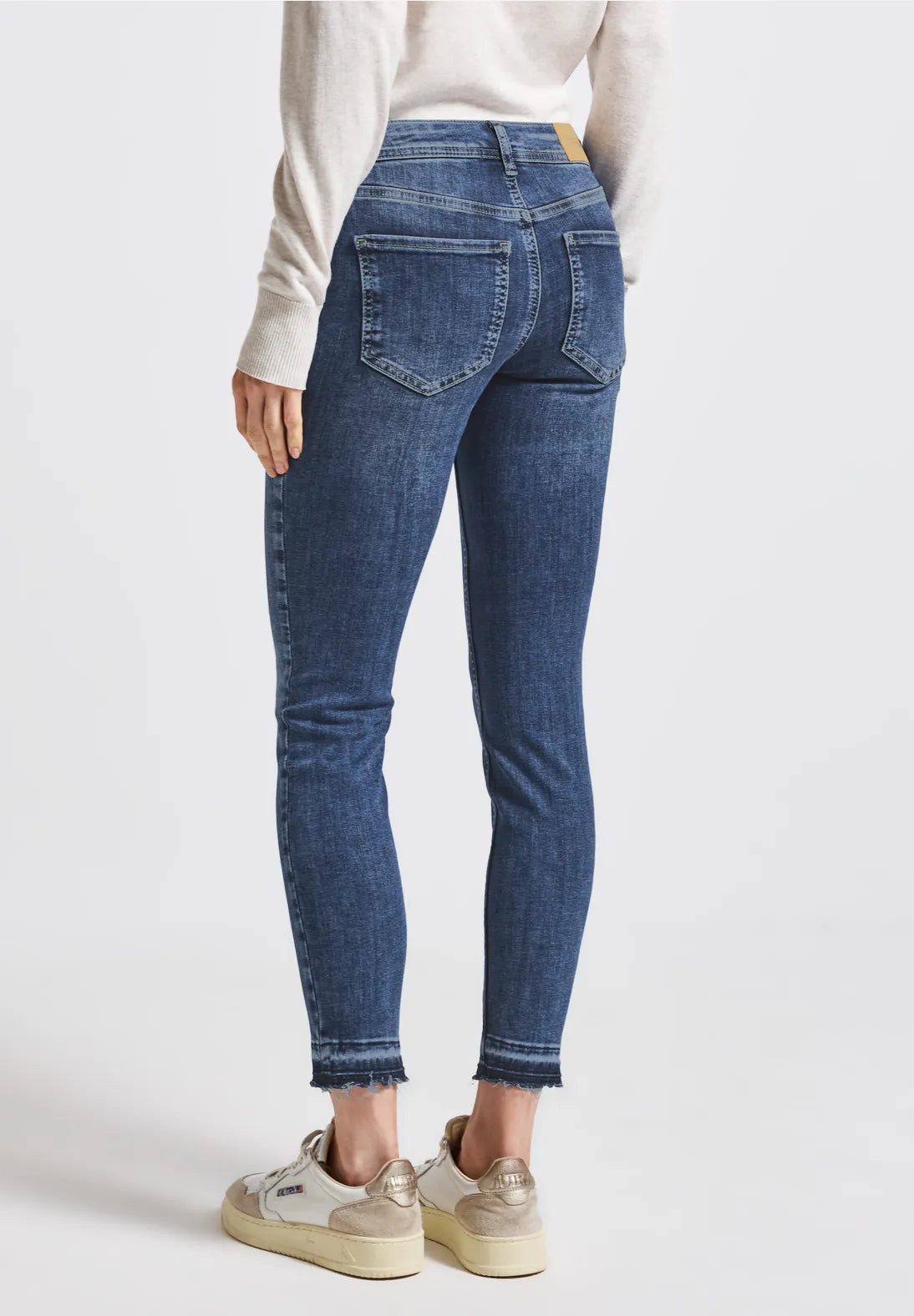 Person wearing blue jeans and a white top on a light gray background