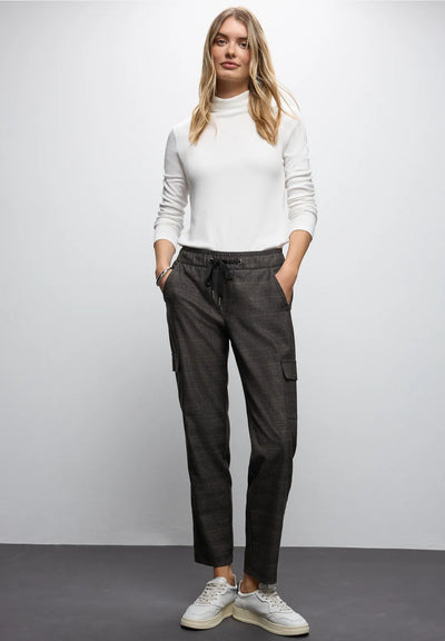 Woman wearing a white turtleneck and dark cargo pants against a plain background