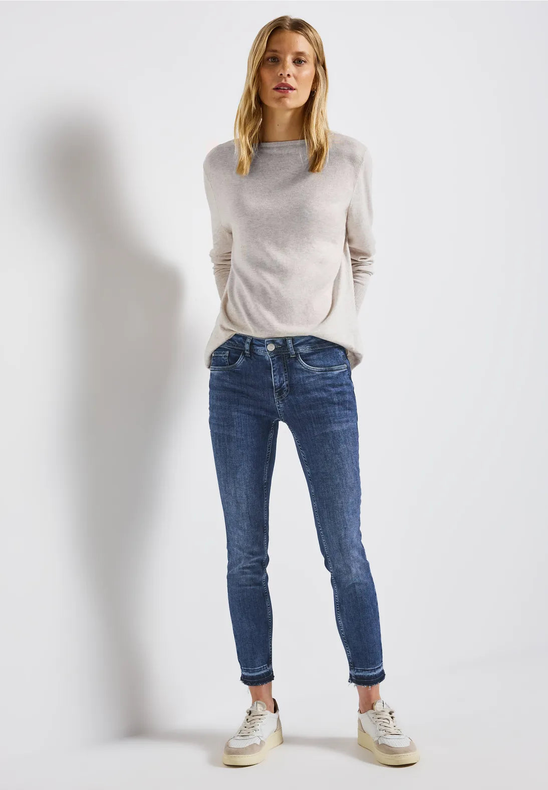 Woman wearing a light gray sweater and blue jeans on a white background