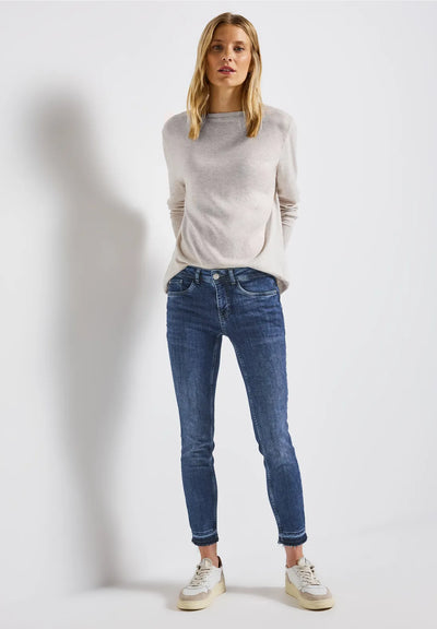 Woman wearing a light gray sweater and blue jeans on a white background