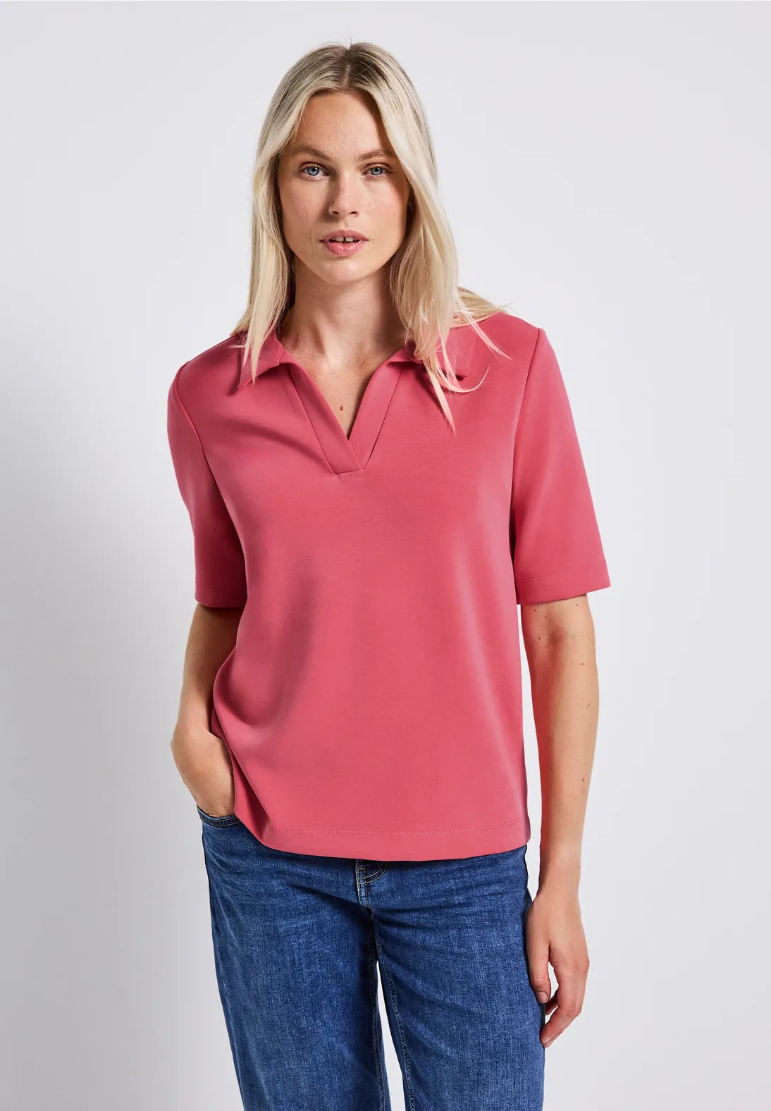 Woman wearing a pink polo shirt and blue jeans on a light gray background