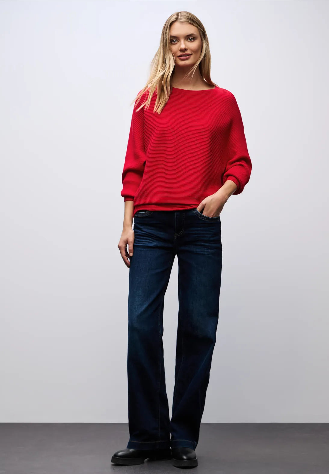Woman wearing a red sweater and blue jeans against a plain background