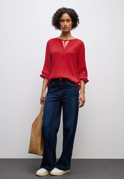Woman wearing a red blouse and blue jeans, holding a brown bag on a plain background