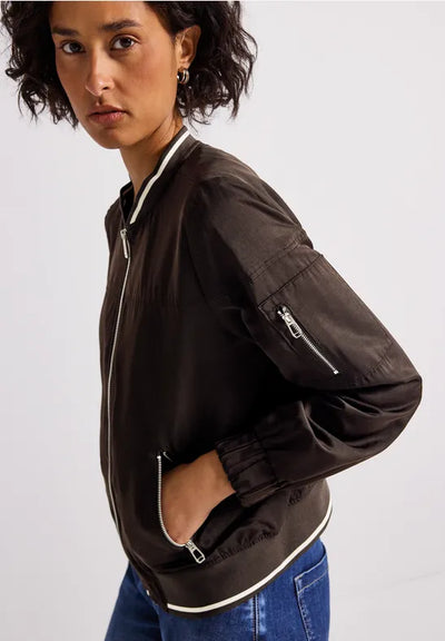 Person wearing a black bomber jacket with white trim on a plain background