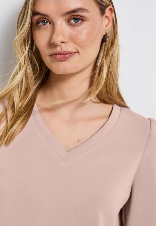 Woman wearing a beige V-neck top against a plain background