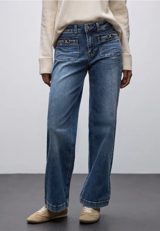 Person wearing blue jeans and a beige sweater on a plain background