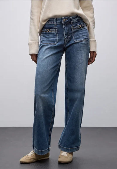 Person wearing blue jeans and a beige sweater on a plain background
