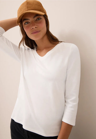 Woman wearing a white top and brown cap against a beige background